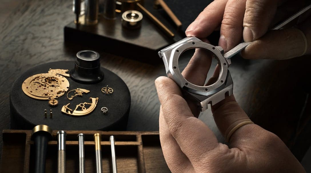 Watchmaker hand-finishing the beveled edge of a stainless-steel octagonal-bezel watch case under warm tungsten light