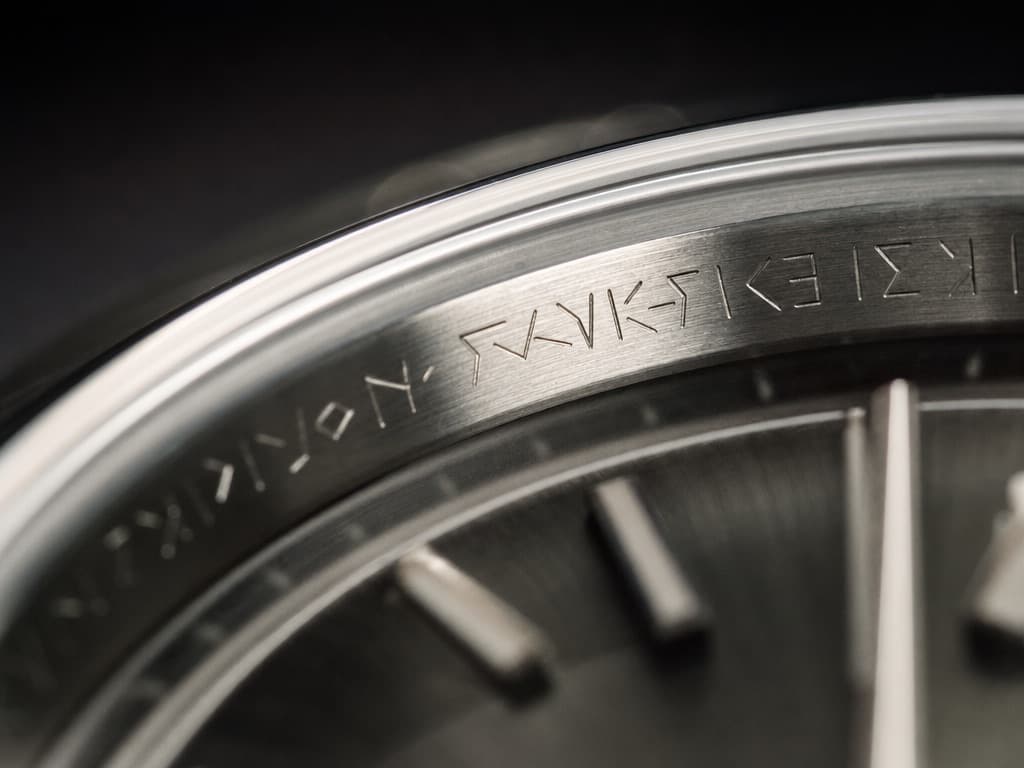 Macro view of fine engraved characters on the polished inner rehaut ring of a stainless-steel watch case