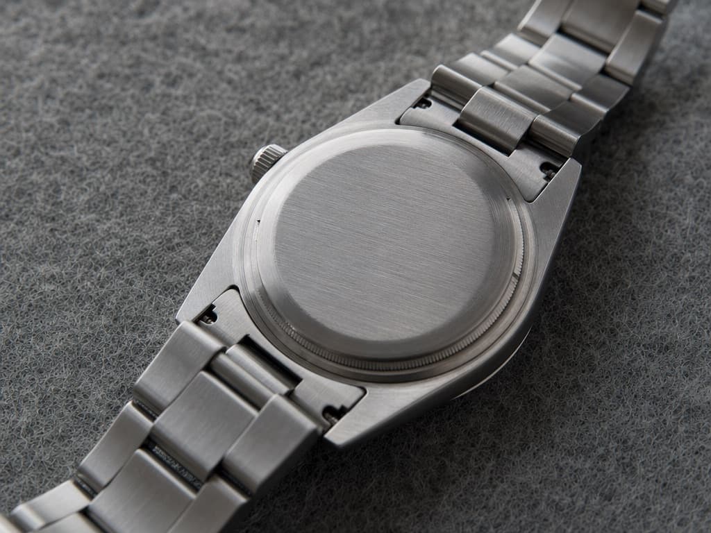 Reverse of a stainless steel sports watch showing a plain smooth brushed caseback with no engraving, beside its solid link bracelet