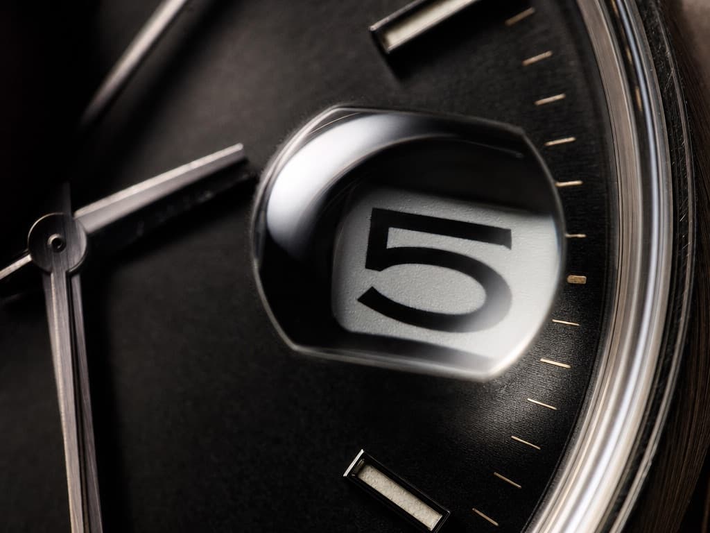 Macro view of a watch date window under a magnifying bubble in the crystal, the numeral enlarged and filling the bubble