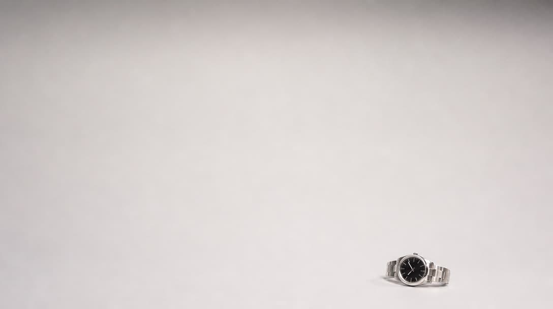 A single small stainless-steel watch lying alone near the corner of a vast empty pale studio surface